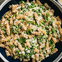 A bowl of rotini pasta with peas, cheese, and basil