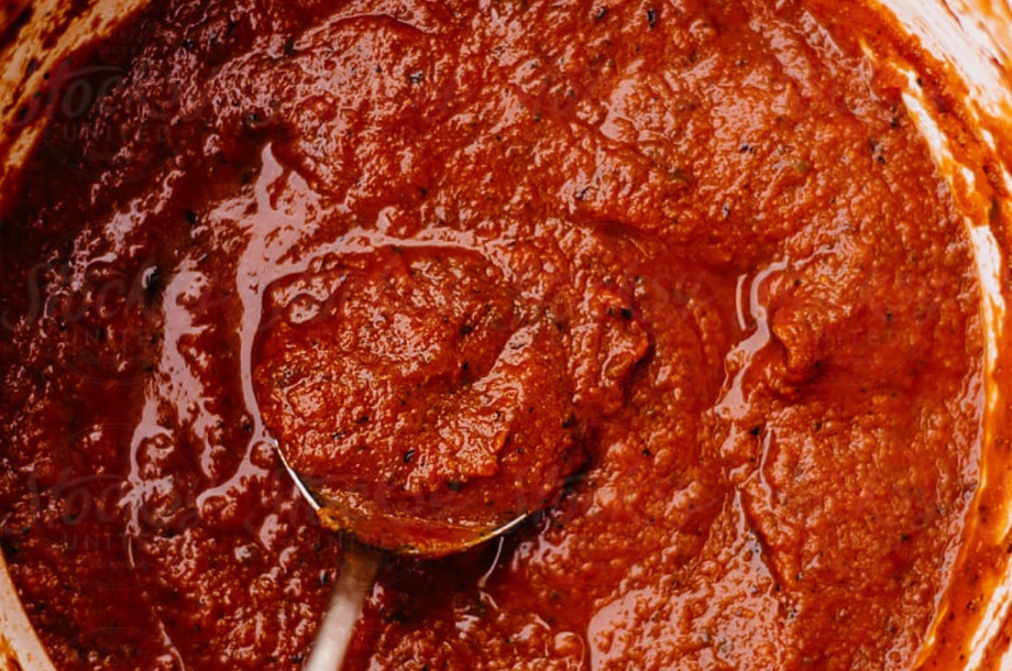 A pot of cooked red tomato sauce with a spoon
