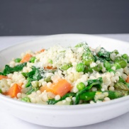 A bowl of pearl couscous topped with spring vegetables, green beans, spinach, green peas, and carrots. Easy, healthy, filling, plant-based, dairy-free, vegan recipe