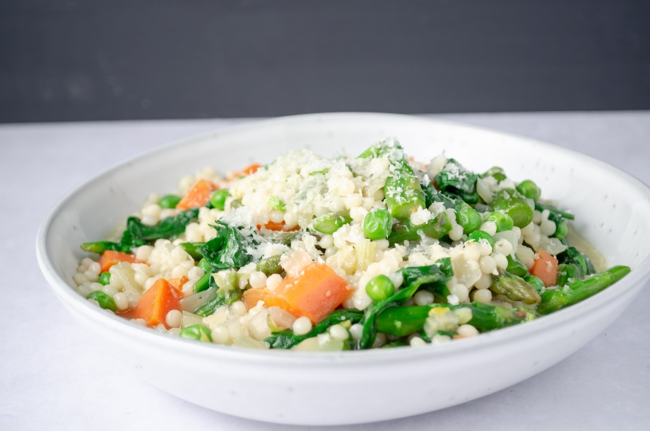 A bowl of pearl couscous topped with spring vegetables, green beans, spinach, green peas, and carrots. Easy, healthy, filling, plant-based, dairy-free, vegan recipe