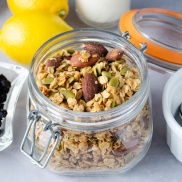 A jar of easy home-made granola made from oats, nuts, pepitas (pumpkin seeds), lemon, blueberry, and coconut
