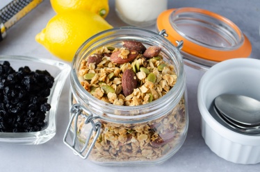 A jar of easy home-made granola made from oats, nuts, pepitas (pumpkin seeds), lemon, blueberry, and coconut