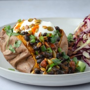 Sweet potato jacket with 15 minute black bean chili stew topped with dairy free yogurt, smoky pepitas, and cilantro and served with a side of coleslaw