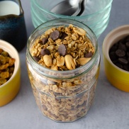 A jar of easy home-made granola made from oats, peanuts, raisins, chocolate chips, honey, and spices served with plant-based milk