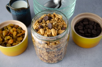 A jar of easy home-made granola made from oats, peanuts, raisins, chocolate chips, honey, and spices served with plant-based milk