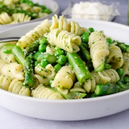 A bowl of pasta with basil pesto and asparagus and peas