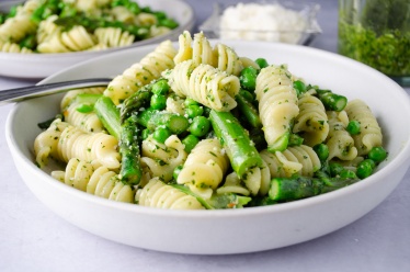 A bowl of pasta with basil pesto and asparagus and peas