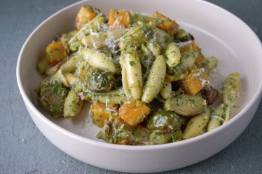 A bowl of kale and basil pesto pasta with butternut squash and roasted Brussel sprouts