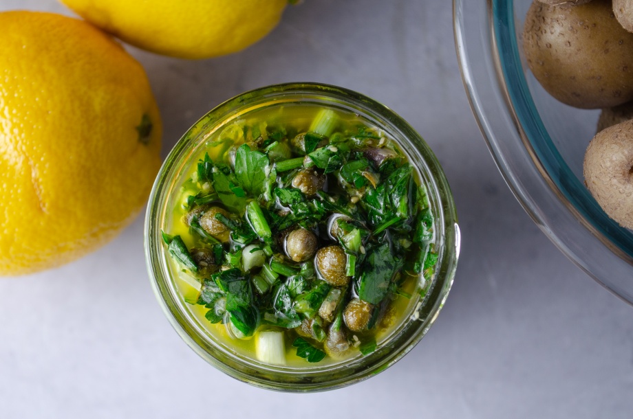 A jar lemon-herb dressing made with lemon, leafy herbs, and capers for topping cauliflower steaks and any other vegetables