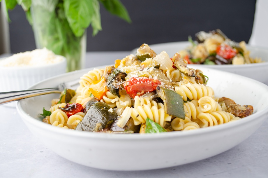 Rotini pasta with parmesean cheese and roasted summer vegetables of squash, zucchini, and eggplant topped with basil