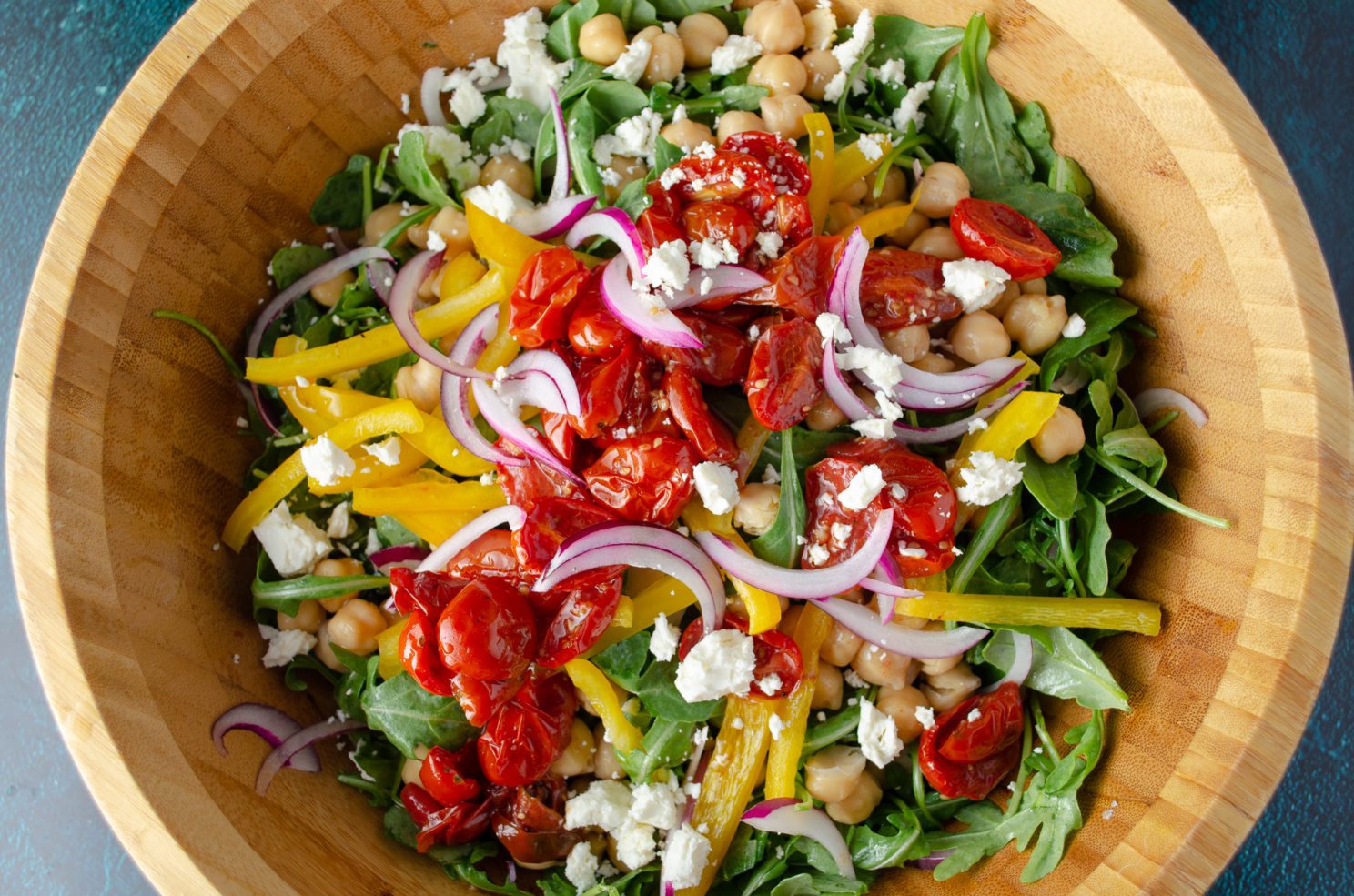 A salad made with arugula, bell peppers, chickpeas, red onion, and roasted cherry tomato confit