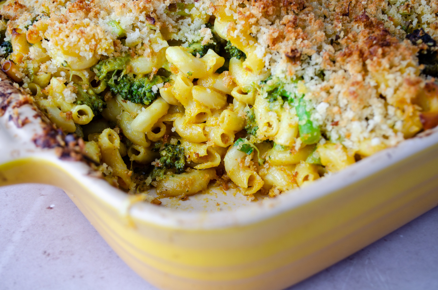 A dish of creamy and cheesy dairy-free, vegan mac and cheese with a crusty breadcrumb topping and broccoli