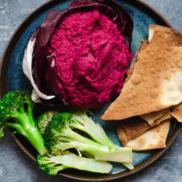 Crimson beet hummus with zingy garlic and lemon flavors in a radicchio bowl served with broccoli and crackers