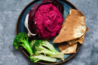 Crimson beet hummus with zingy garlic and lemon flavors in a radicchio bowl served with broccoli and crackers