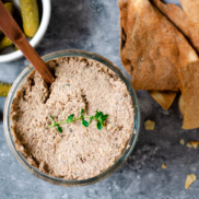 A bowl of plant-rich mushroom pate with a side of pita chips and cornichons