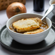A warm, inviting bowl of festive, vegan French Onion Soup topped with crusty bed and cheese- perfect for holidays or Christmas