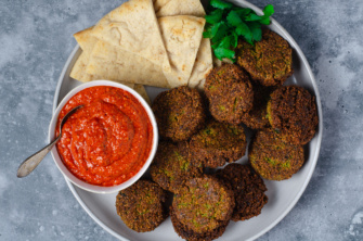 A hearty plate of plant-based falafel with romesco sauce that's sweet, tangy, and zippy,served with pita bread