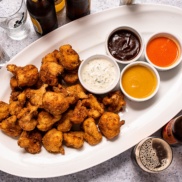 A tray of fried cauliflower "wings" for a plant-based superbowl appetizer with dipping sauces