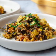 A bowl of black bean and rice gratin topped with crunchy tortilla chips and herbs, a protein-full plant-based dinner idea