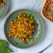 A bowl of chickpea and pearl couscous gratin flavored with curry inspired flavors and topped with cilantro and chopped almonds for a satisfying plant-based dinner idea