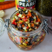 A jar of carnivale olive tapenade made with beautiful, fun colors and flavors of black olives, pimento stuffed olives, green olives, capers, and roasted red peppers