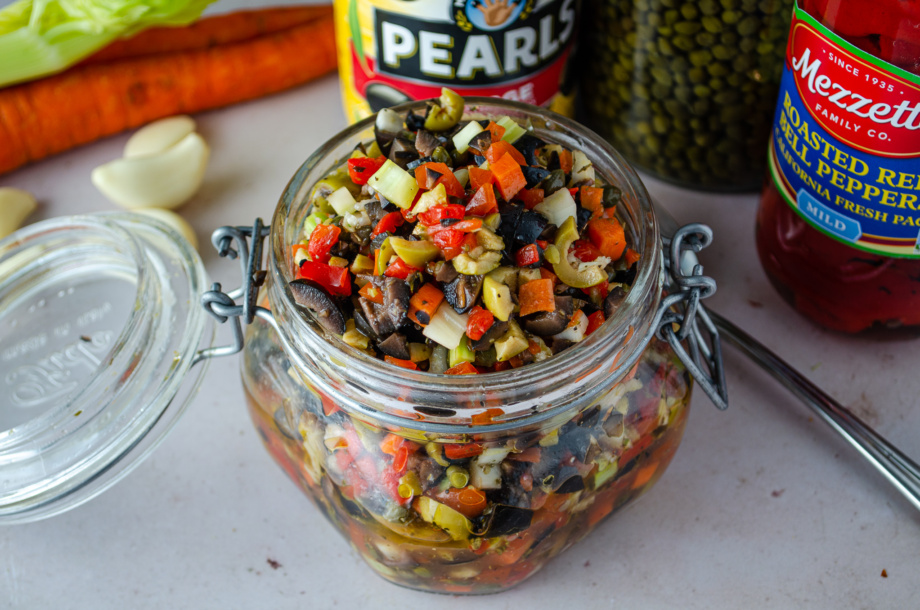 A jar of carnivale olive tapenade made with beautiful, fun colors and flavors of black olives, pimento stuffed olives, green olives, capers, and roasted red peppers