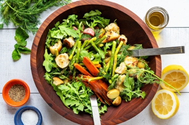 A big wood bowl of panzanella salad with Roasted Spring Vegetables of potato, asparagus, cucumber, and radish, topped with olive oil, lemon juice, salt, pepper, and fresh herbs like dill or mint