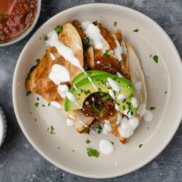 Plant-based quesadillas made with refried beans, vegetables, and salsa topped with avocado, dairy-free sour cream, and cilantro