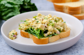 A piece of bread topped with lettuce and a scoop of of vegan, plant-based "egg" salad made with all the classic flavors and ingredients but with silken tofu instead of egg