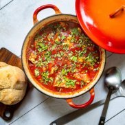 A plant-based shakshuka in a red le creuset pot topped with herbs and served with homemade bread