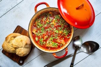 A plant-based shakshuka in a red le creuset pot topped with herbs and served with homemade bread