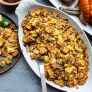 A dish of thanksgiving cornbread stuffing shown alongside a feast of plant-based stuffed pumpkins