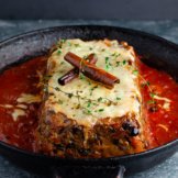 A slice of the a plant-based holiday roast in salsa rossa and topped with cinnamon sticks